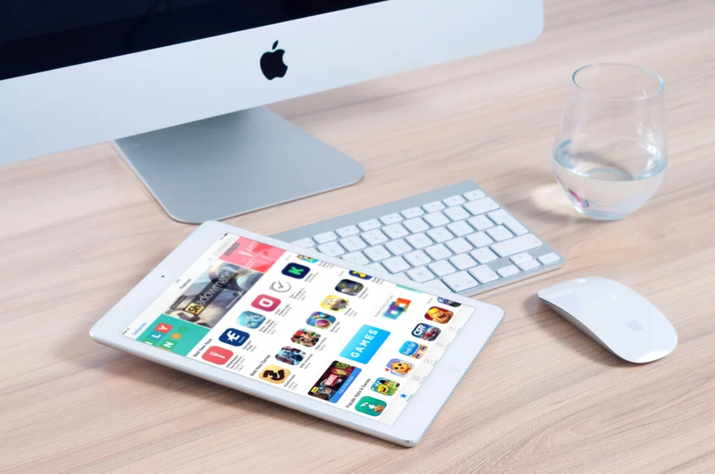Bureau avec iMac, iPad affichant l’App Store, clavier Apple, souris et verre d’eau.