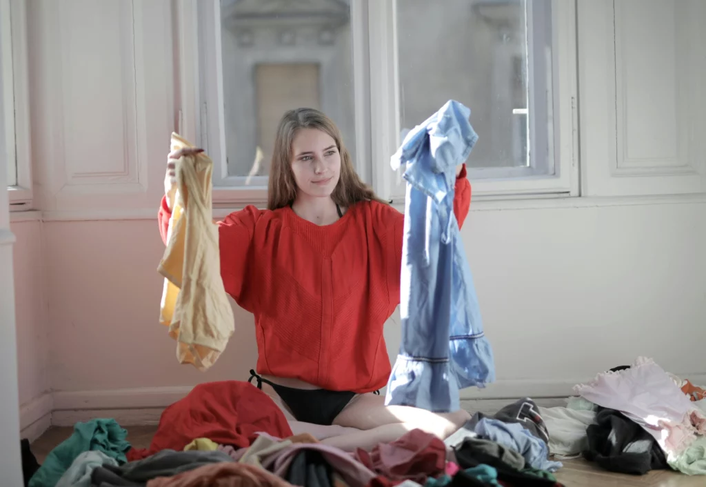 Femme comparant deux vêtements, un jaune et un bleu, au milieu d’un tas de vêtements.
