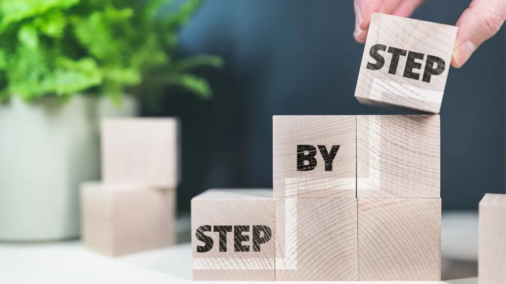 Construire la réussite pas à pas - iterates Main empilant des blocs en bois gravés des mots “Step by Step” dans un concept de progression.
