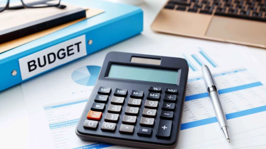 Calculatrice posée sur des documents financiers avec un classeur bleu marqué "Budget".