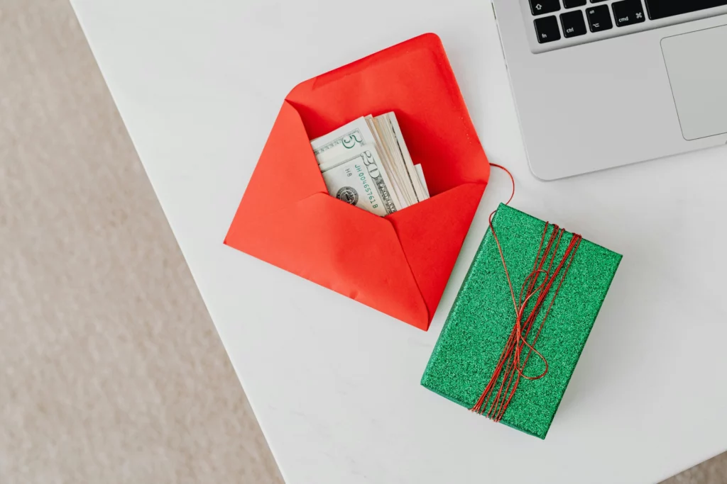 Cadeau en argent liquide dans une enveloppe rouge - iterates Enveloppe rouge contenant des billets de banque à côté d’un cadeau vert scintillant.