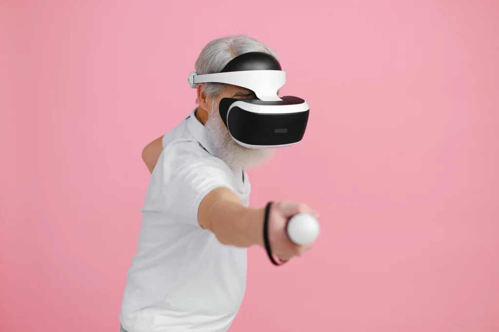 Expérience immersive en réalité virtuelle pour les seniors - iterates Homme âgé utilisant un casque de réalité virtuelle et une manette sur fond rose.
