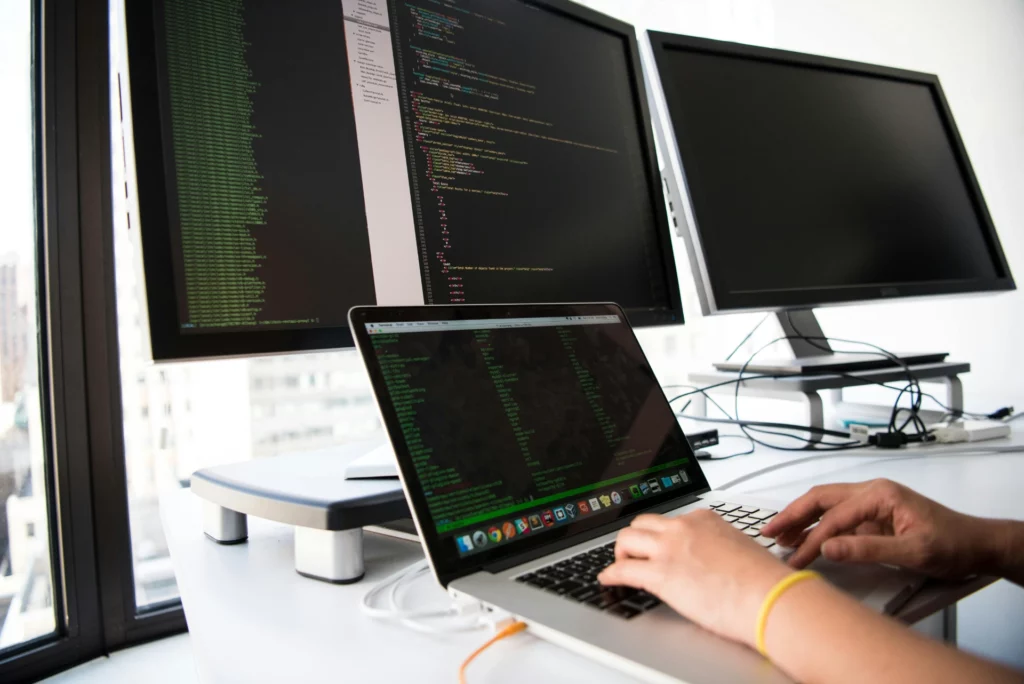 Personne tapant du code sur un ordinateur portable avec plusieurs écrans affichant du code.
