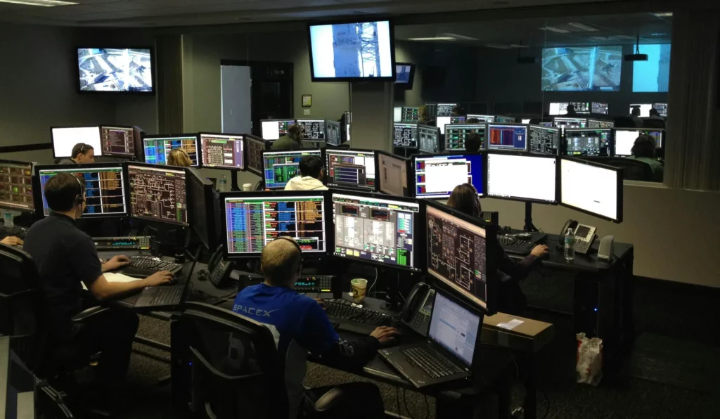 Salle de contrôle informatique avec plusieurs opérateurs surveillant des écrans de données complexes.