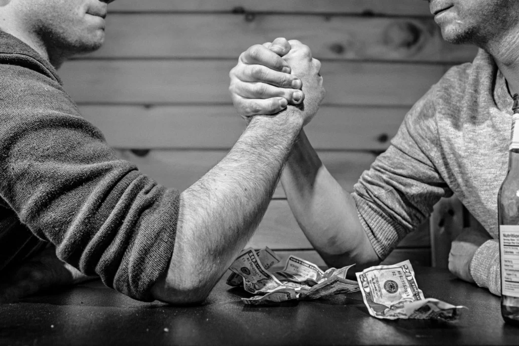 Deux hommes font un bras de fer avec des billets de dollars posés sur la table.