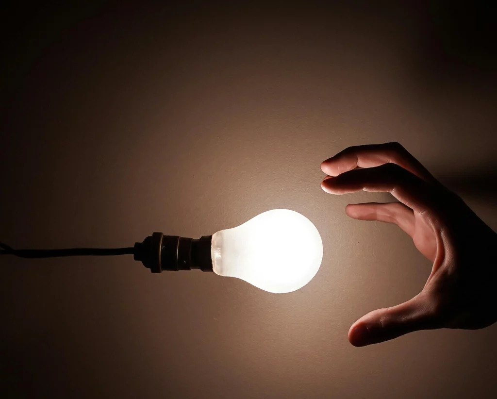 Main tendue vers une ampoule allumée, symbolisant l'idée de création ou d'innovation.