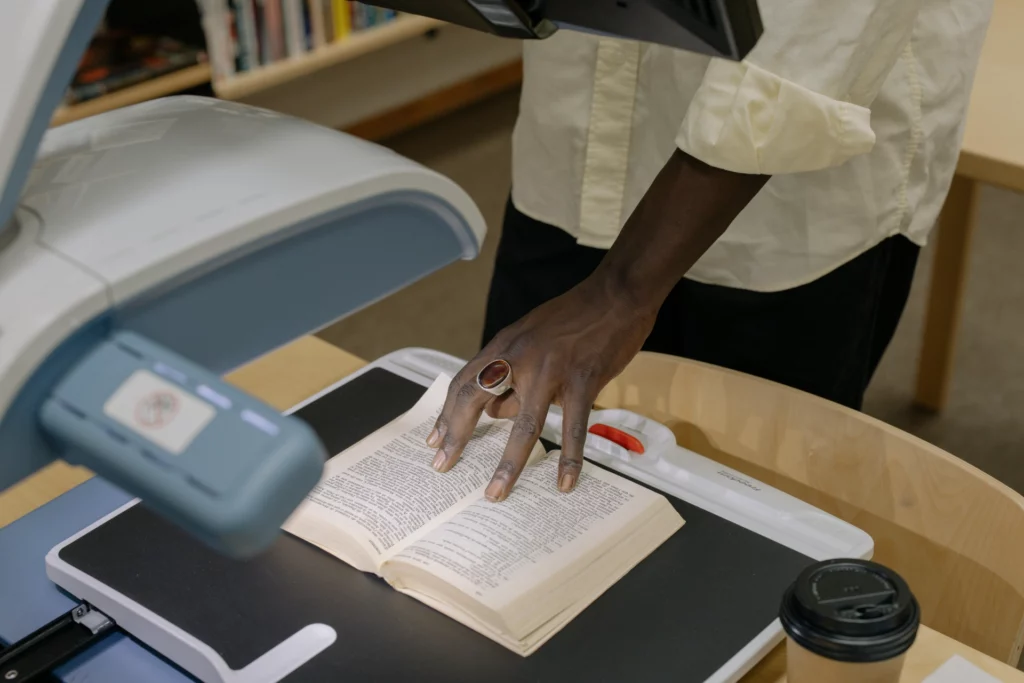 Numérisation d’un livre avec un scanner en bibliothèque - iterates Main d’une personne utilisant un scanner pour numériser un livre ouvert dans une bibliothèque.