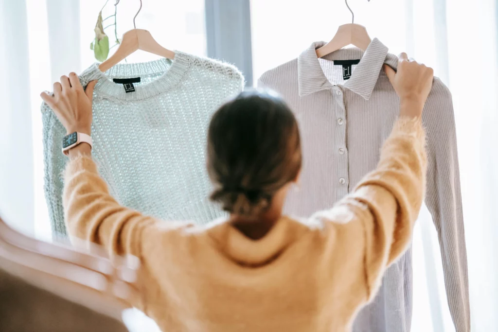 Une personne comparant deux vêtements accrochés sur des cintres pour choisir lequel porter.
