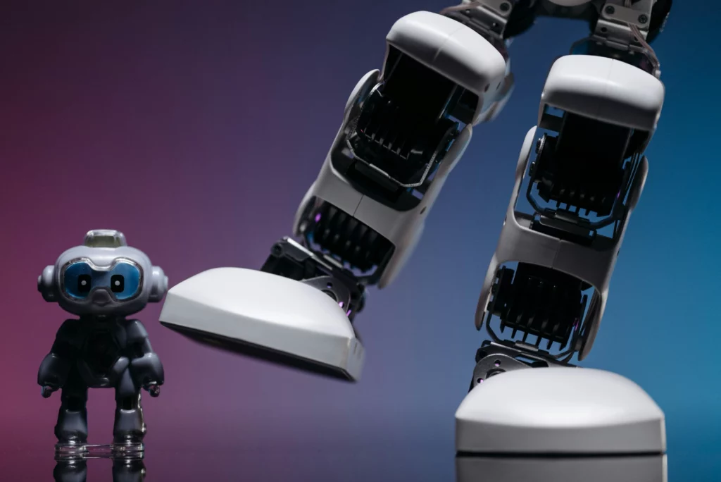 Petit robot et grand robot humanoïde côte à côte - iterates Petit jouet robot à côté de grandes jambes de robot humanoïde sur fond dégradé bleu-violet.