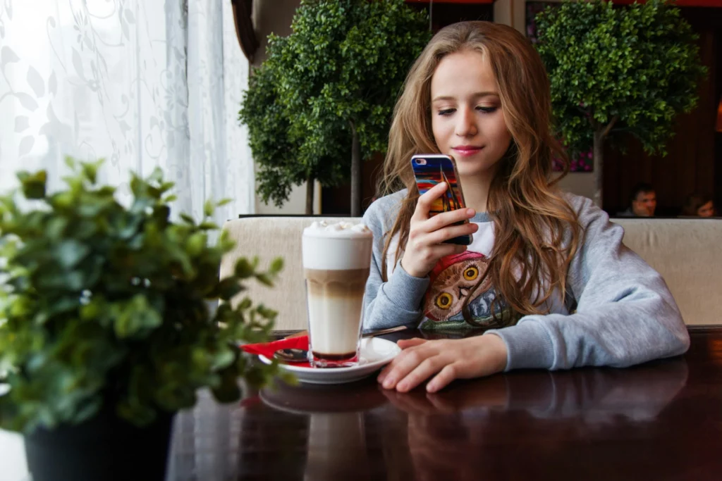 Pause café et smartphone dans un café chaleureux - iterates Jeune femme regardant son smartphone en buvant un café dans un café cosy.