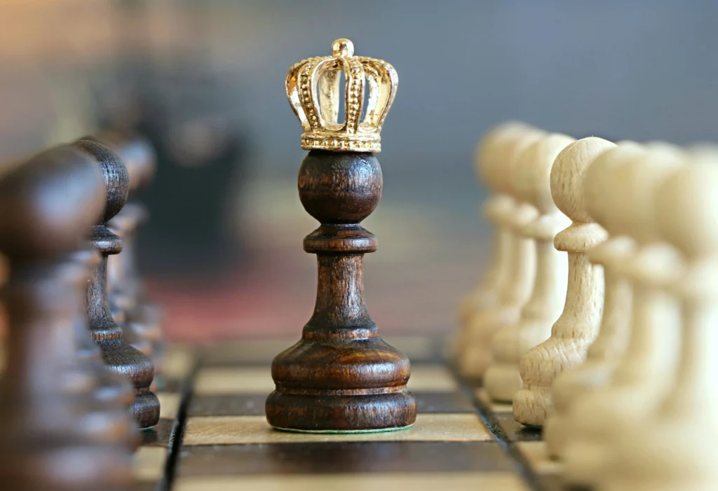 Pion couronné symbolisant la promotion aux échecs - iterates Pion d’échecs en bois foncé coiffé d’une couronne dorée sur un échiquier.