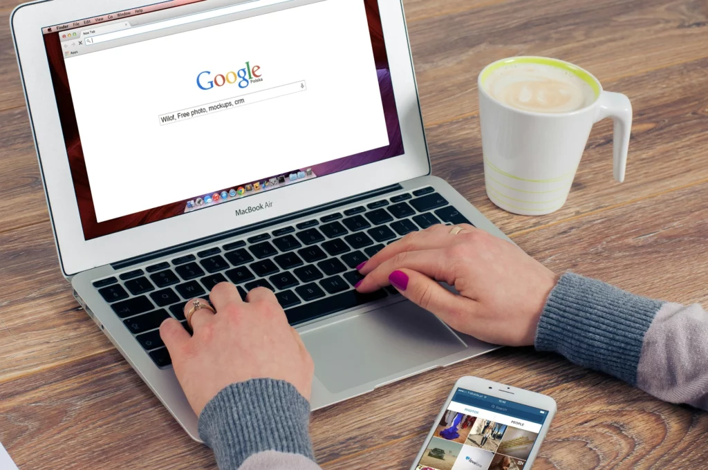 Personne utilisant un ordinateur portable MacBook pour effectuer une recherche Google avec une tasse de café à côté.