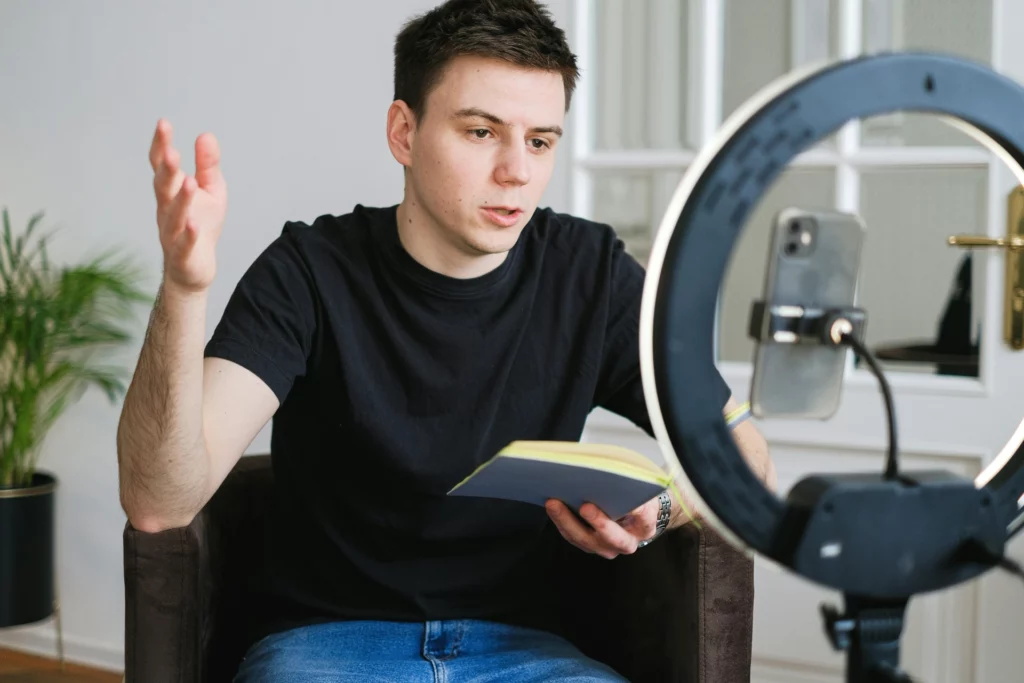 Un jeune homme lit un livre tout en s'exprimant devant une caméra avec un éclairage annulaire.