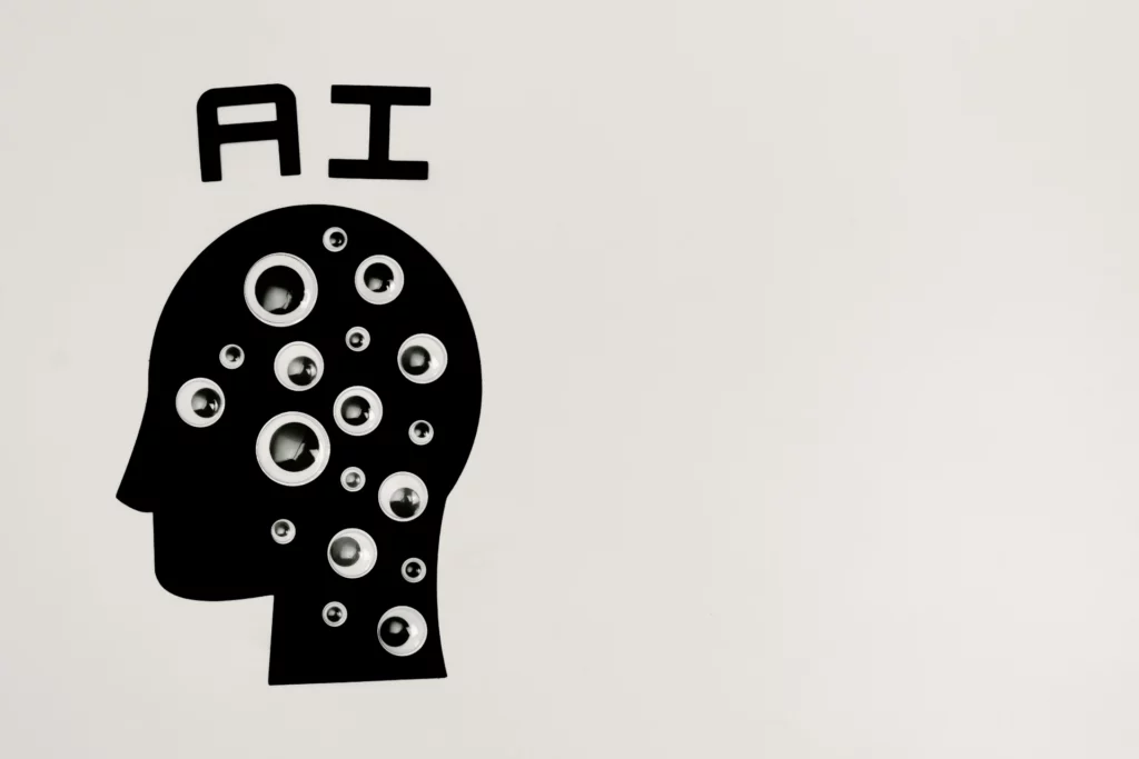 Représentation de l’intelligence artificielle avec une tête stylisée - iterates Illustration d’une tête humaine noire remplie d’yeux et du texte « AI » sur fond blanc.