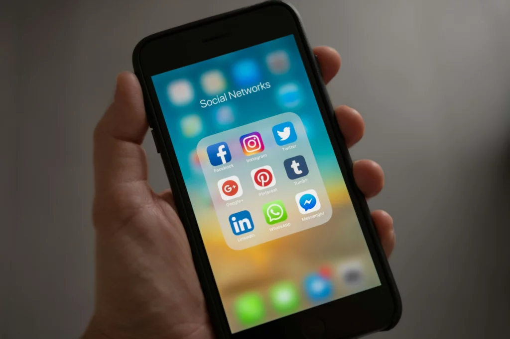 Main tenant un smartphone affichant des icônes d’applications de réseaux sociaux.