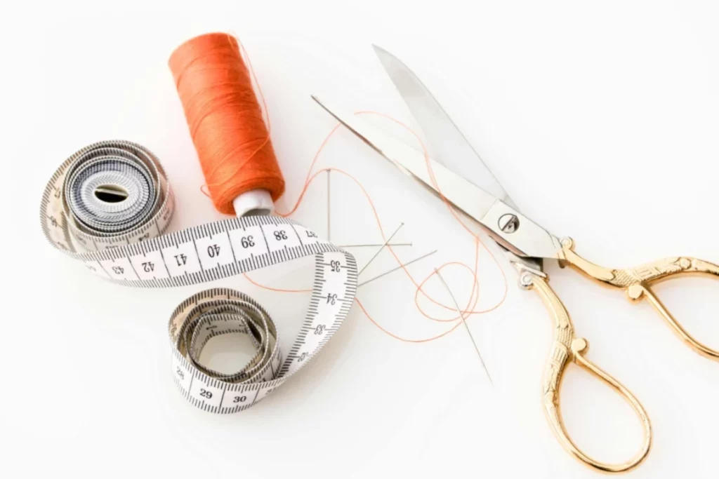 Matériel de couture et accessoires de confection - iterates Outils de couture avec fil orange, mètre ruban, aiguilles et ciseaux dorés.