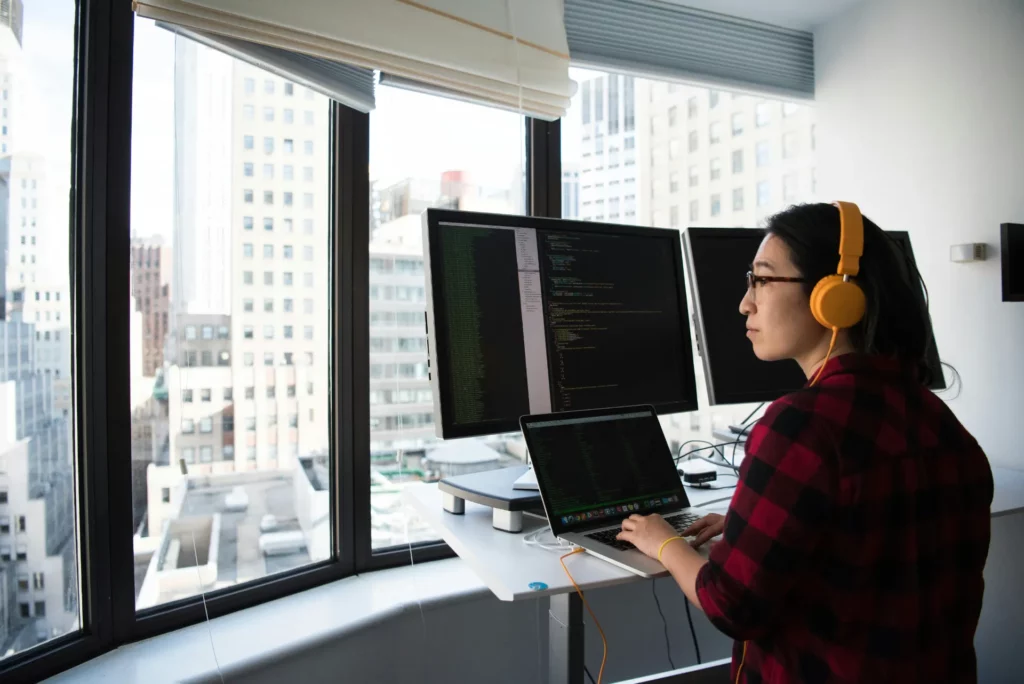 Développeuse codant sur ordinateur avec plusieurs écrans dans un bureau en hauteur.