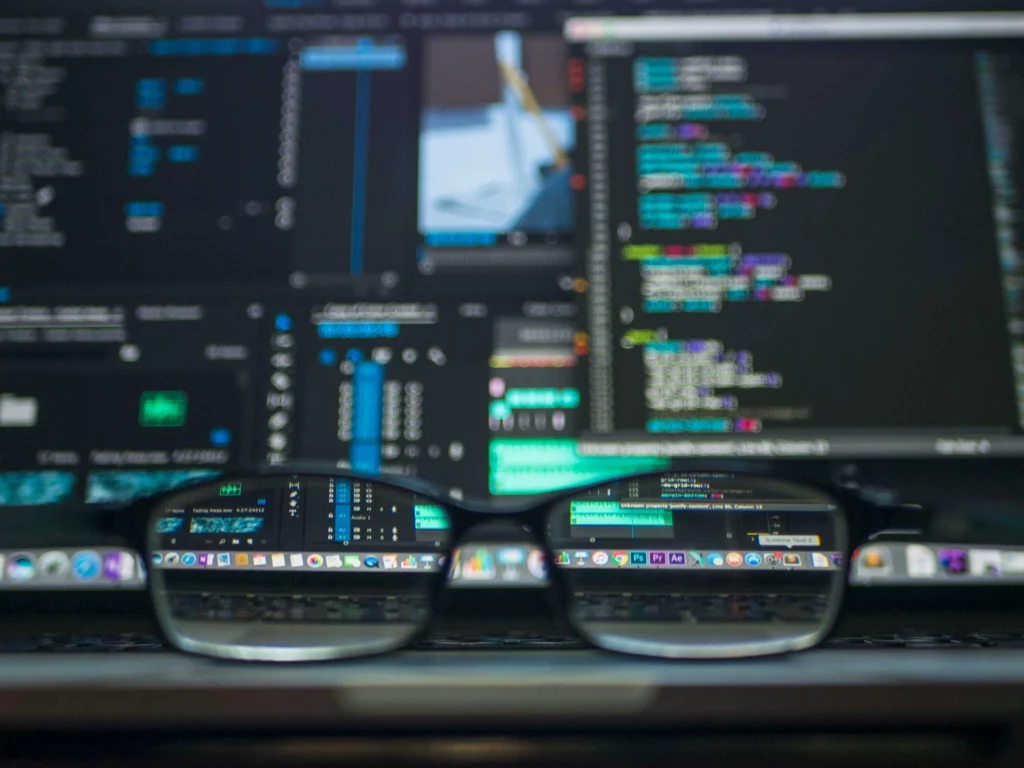 Lunettes posées devant un écran d’ordinateur affichant du code et des interfaces logicielles.