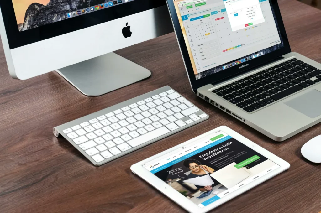 Poste de travail digital avec équipements Apple pour la gestion de projets web - iterates Ordinateur de bureau, MacBook et tablette affichant des interfaces de gestion de projet sur un bureau en bois.