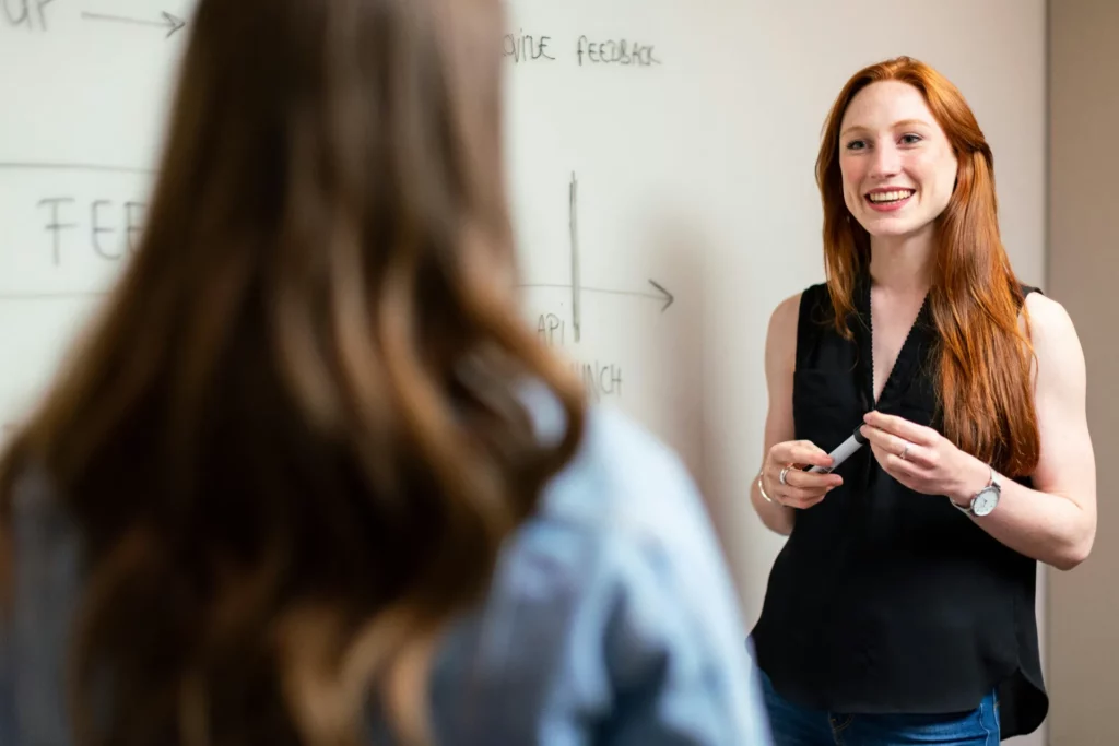 Professionnelle souriante expliquant un concept sur un tableau blanc lors d’une réunion.