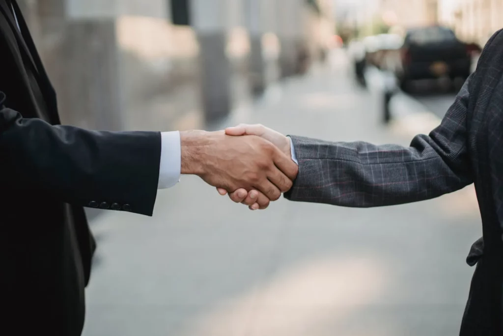 Poignée de main entre deux professionnels en costume sur un trottoir urbain.