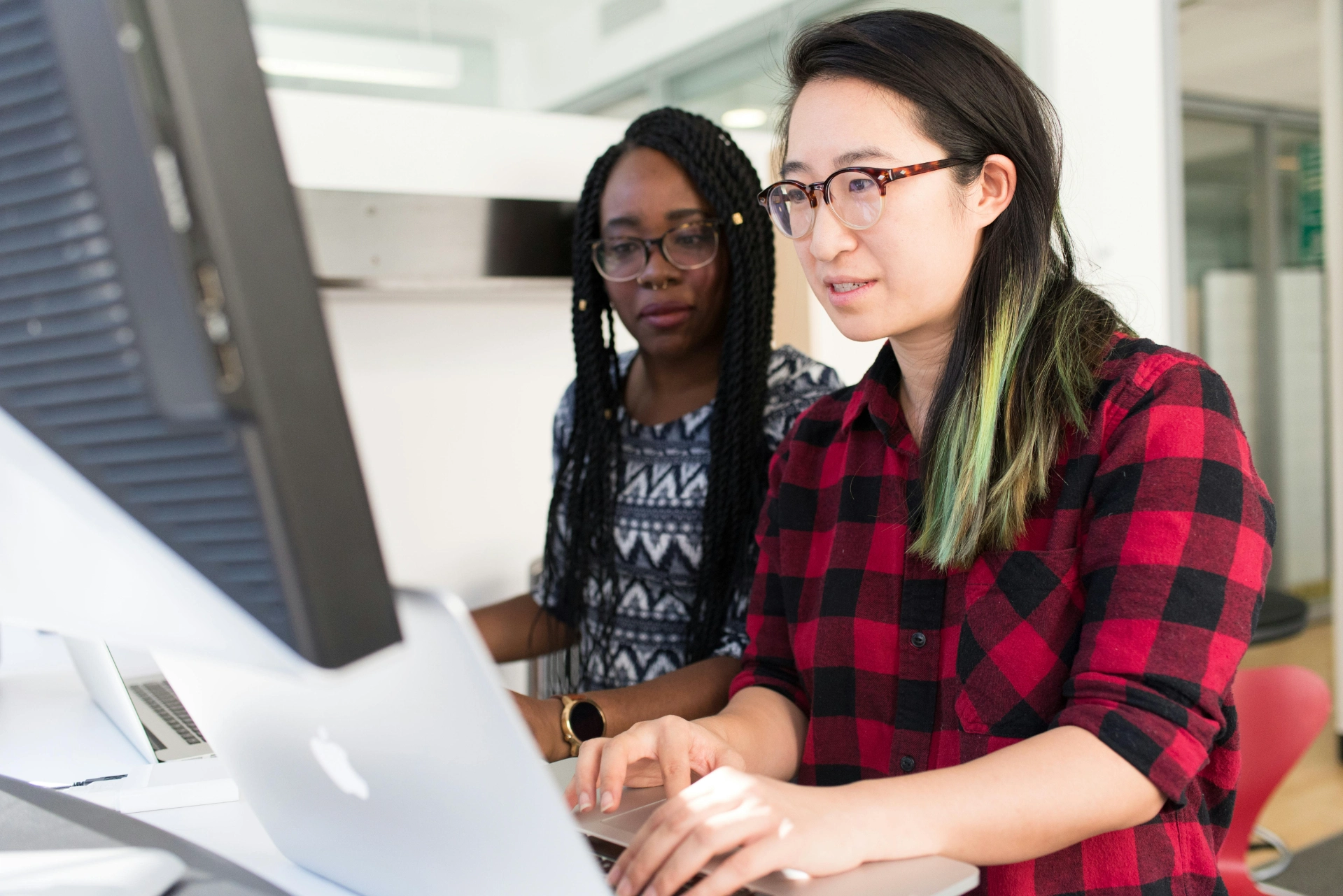 Collaboration between colleagues on a digital project - iterates Two women working together on a computer in a modern office.