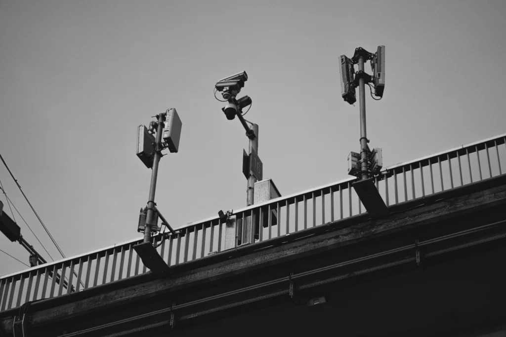 Surveillance urbaine - iterates Des caméras de surveillance et des équipements de communication montés sur un pont, observant la zone en dessous.