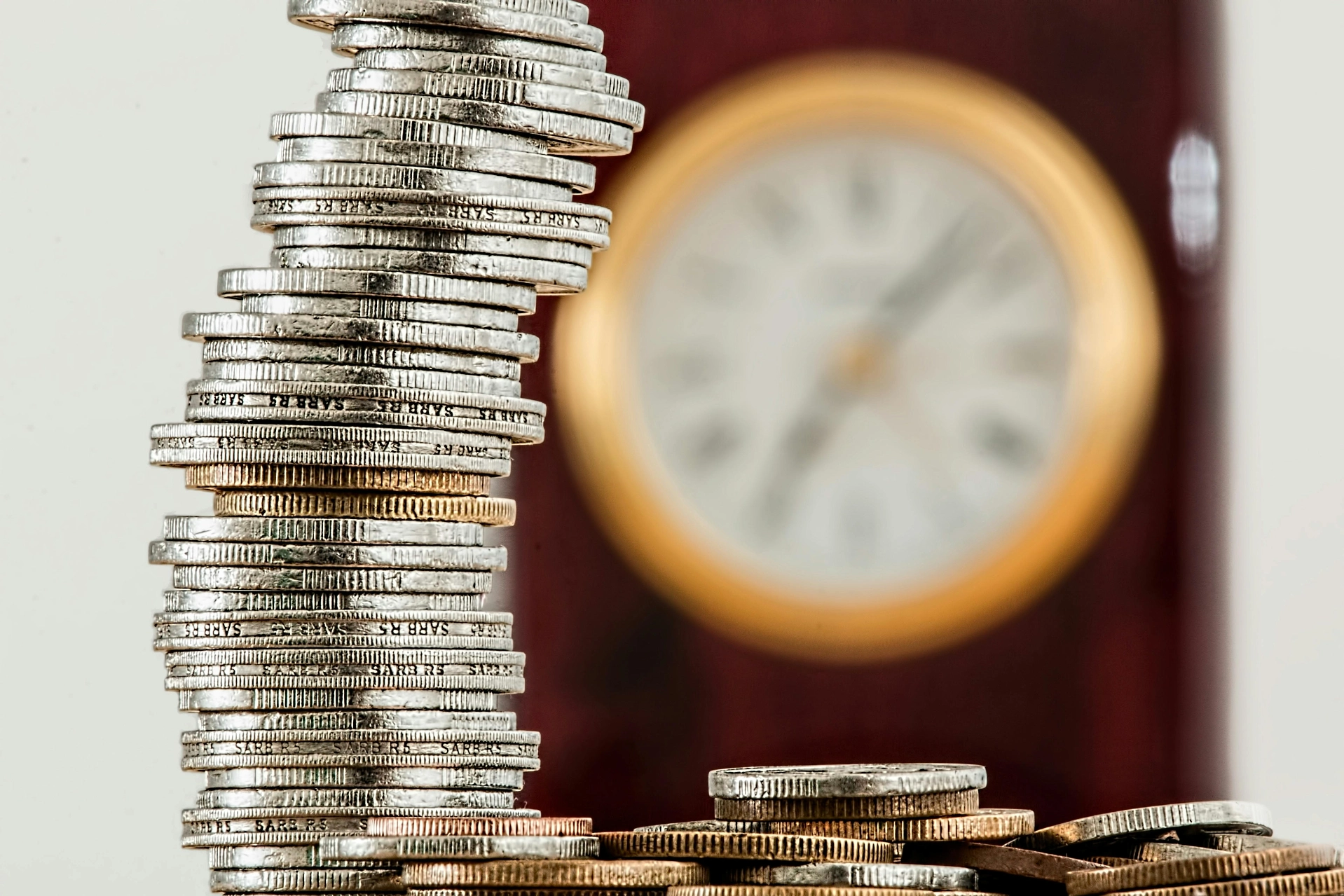 Stack of coins and clock symbolising time and money - iterates Stack of tilted coins with a blurred clock in the background.