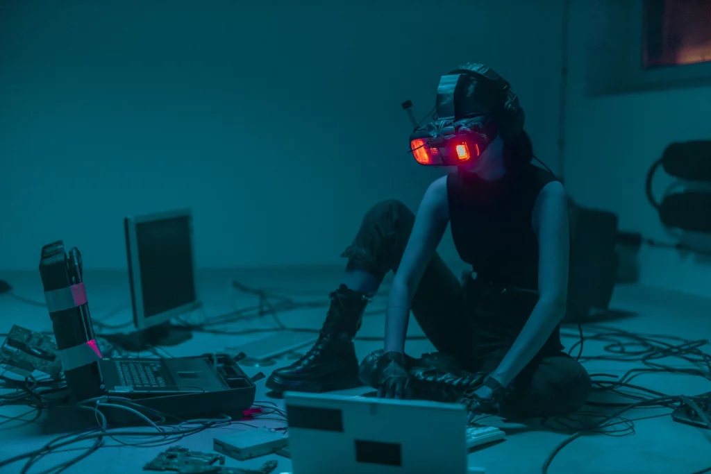 Femme avec un casque de réalité virtuelle rouge entourée d’équipements informatiques dans une pièce sombre.