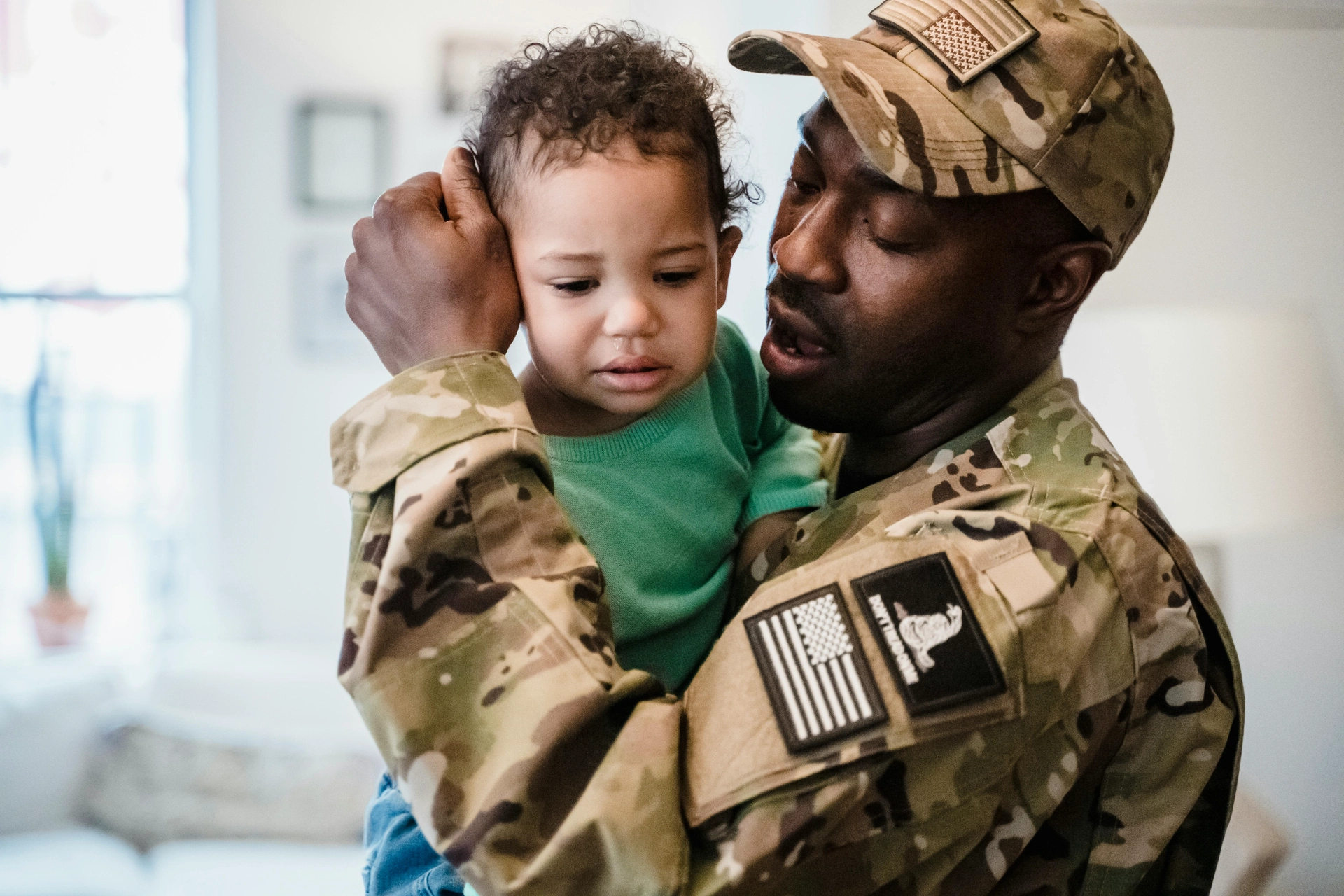 - iterates Soldier in uniform tenderly holding a child at home.
