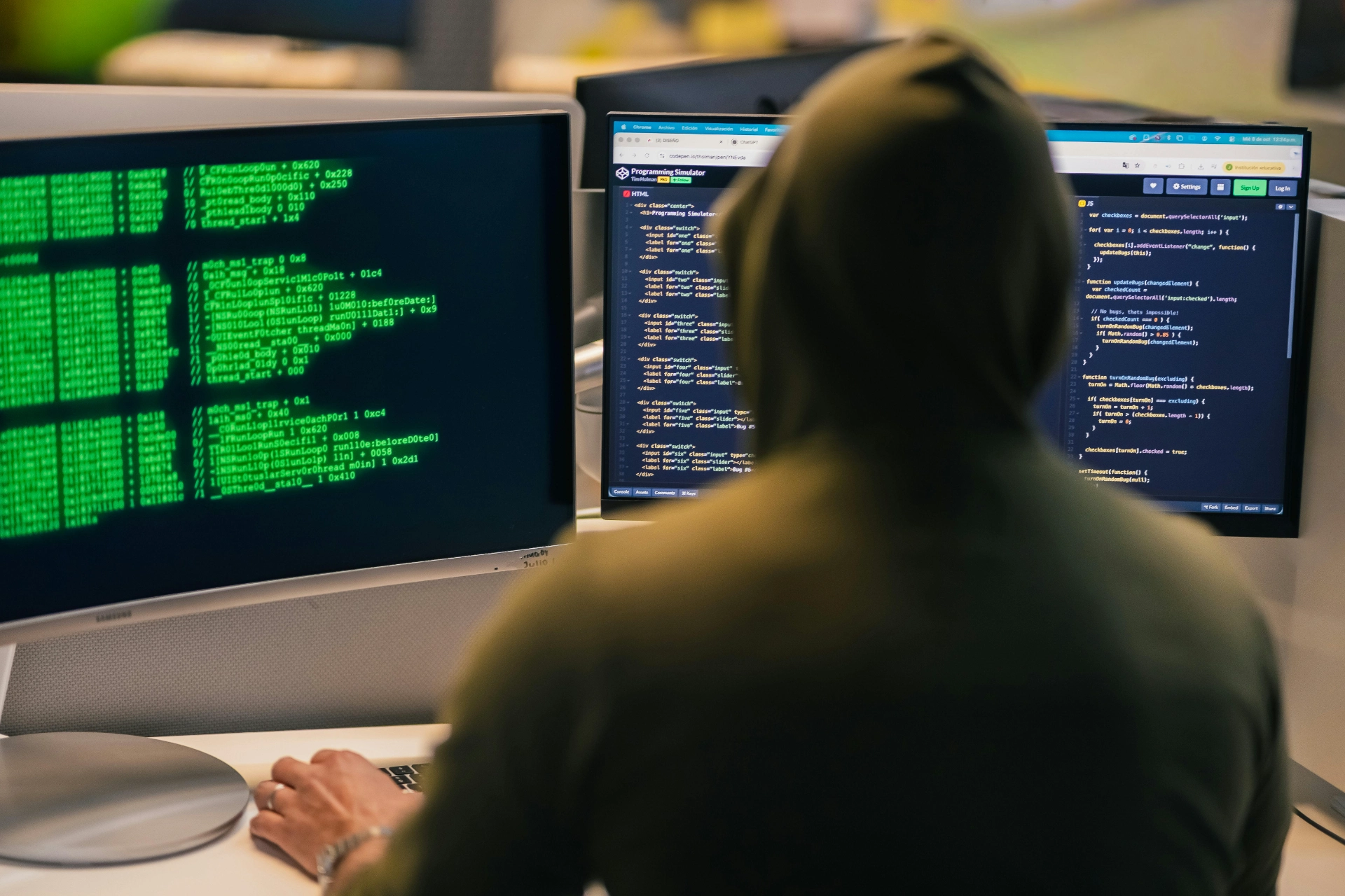 - iterates A person in a hoodie in front of two screens displaying computer code and data in green.
