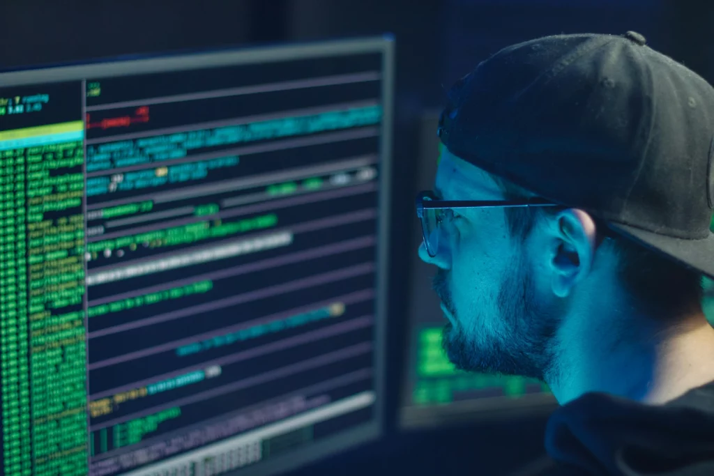 Ingénieur en cybersécurité analysant des lignes de code sur un double écran lors d’une intervention après une attaque informatique.
