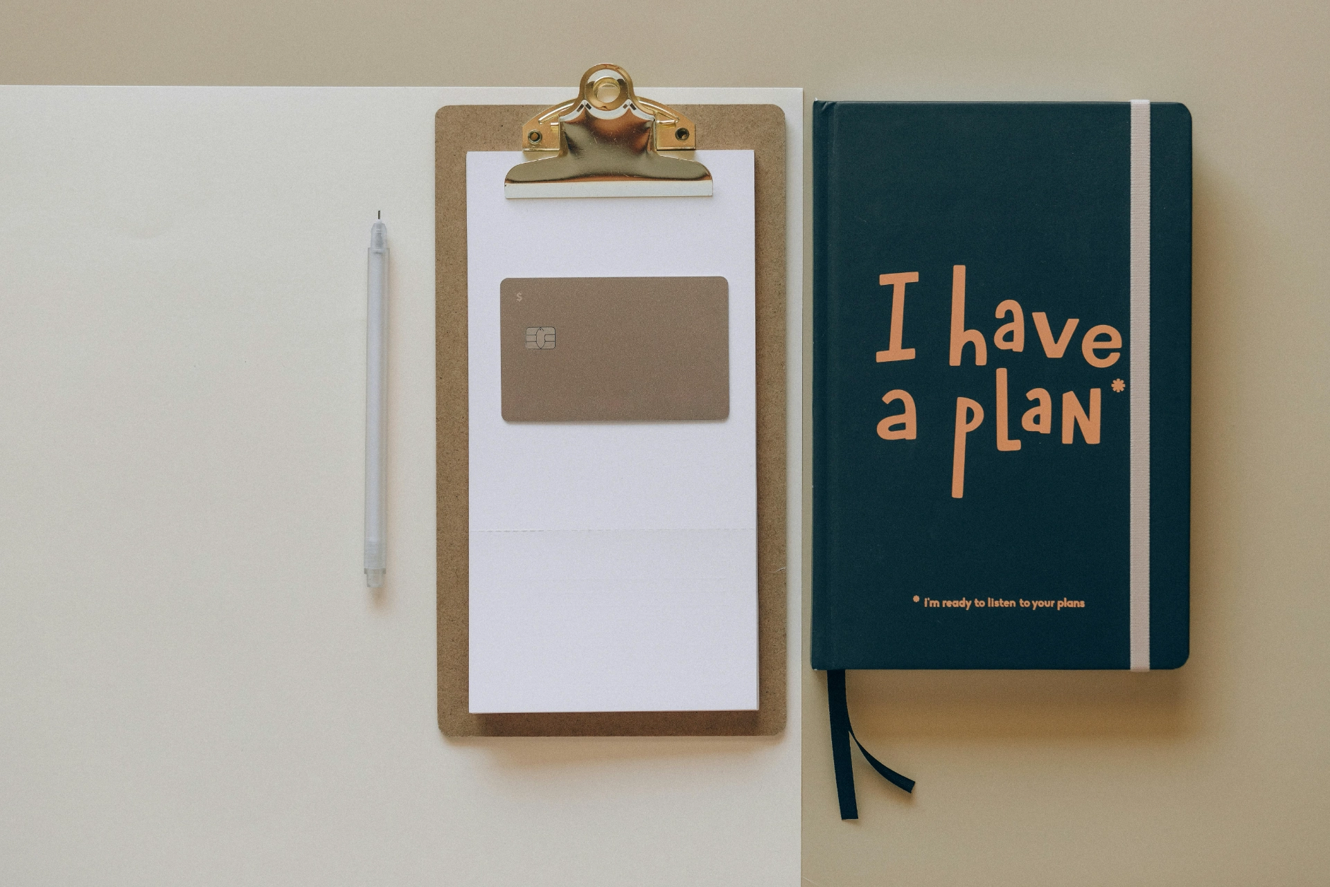 - iterates Notebook "I have a plan", bank card, notepad and pen on a desk.