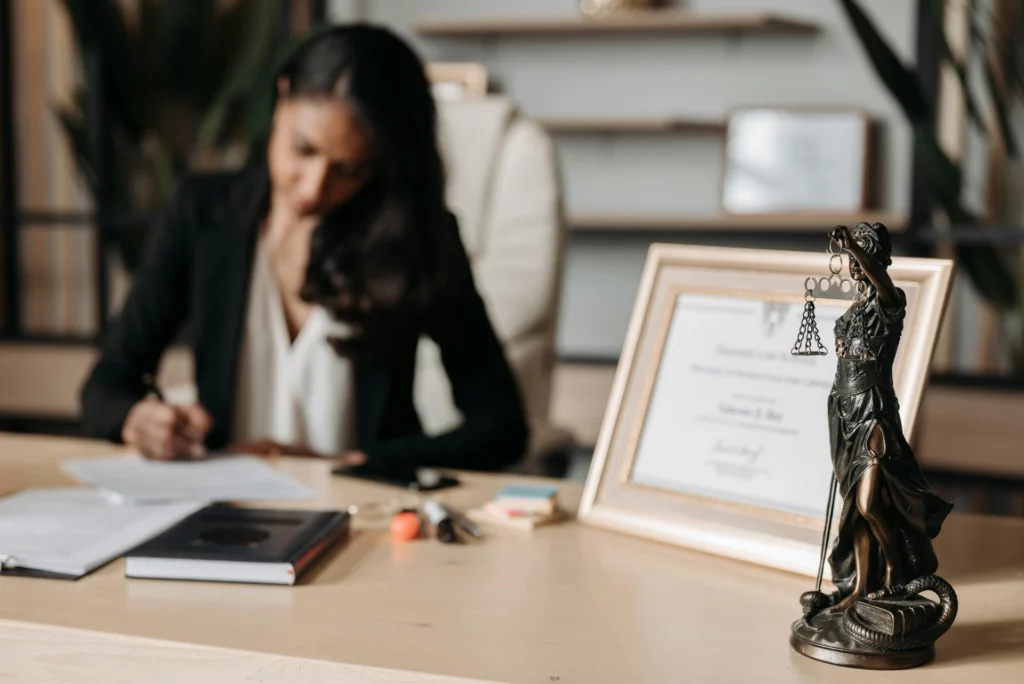 Expertise juridique et protection des droits - iterates Avocate rédigeant un document dans son bureau, avec une statue de la justice et un diplôme en arrière-plan.