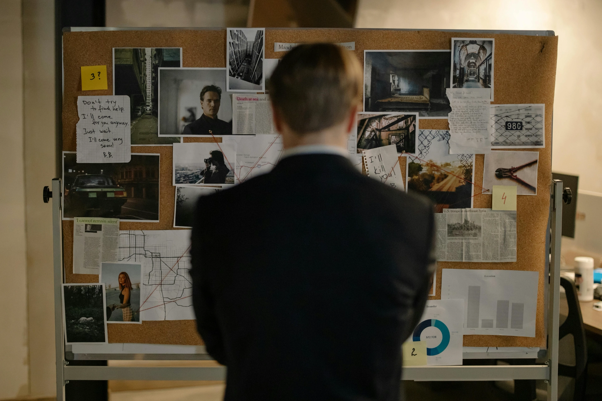 A man in a suit looking at a survey board filled with photos and notes.