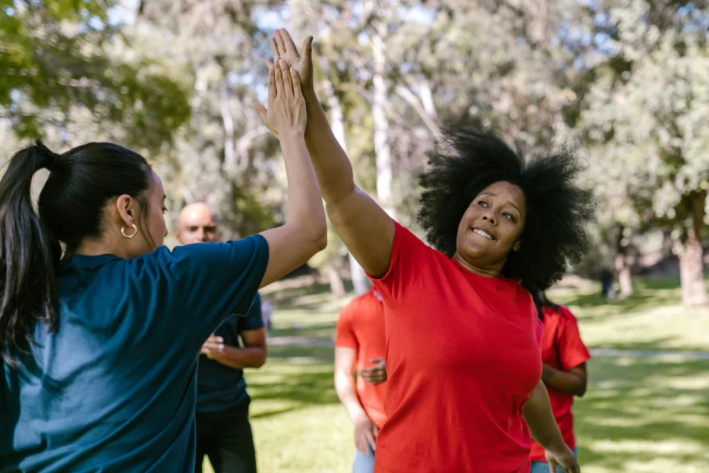 Célébrer la réussite collective autour de la conformité NIS2 - iterates Deux femmes se félicitent d’un high five lors d’une activité d’équipe en plein air.