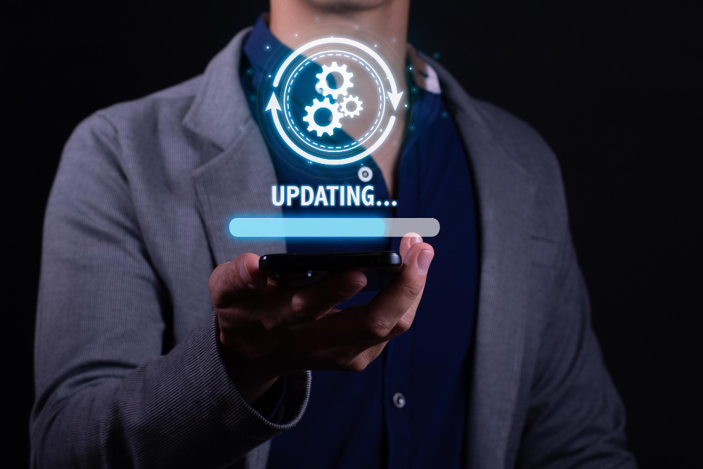 Person wearing a blazer holds a smartphone with a glowing holographic 'UPDATING...' progress bar and gear icons above the screen.