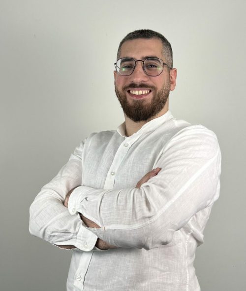 Portrait professionnel de Marc Srouji, développeur souriant en chemise blanche et lunettes, bras croisés.